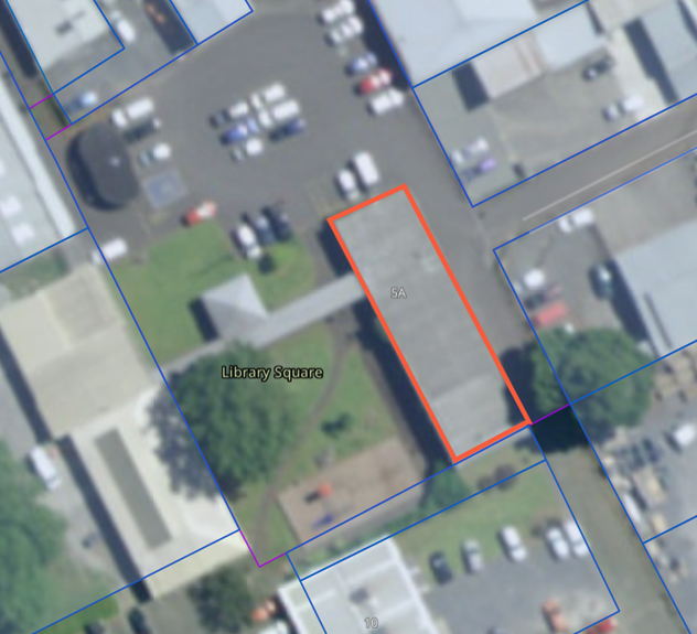 Aerial satellite image of a mixed-use area showing buildings, parking lots, and roads, with one long rectangular building outlined in orange and labeled &ldquo;5A,&rdquo; adjacent to a green space labeled &ldquo;Library Square,&rdquo; and surrounding property boundaries marked in blue.
